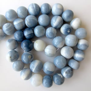 May include: A strand of blue and white opal beads. The beads are round and have a smooth, polished finish. They are strung on a clear thread.