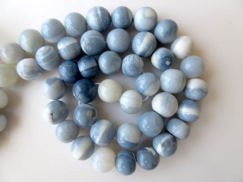 May include: A strand of blue and white opal beads. The beads are round and have a smooth, polished finish. They are strung on a clear thread.