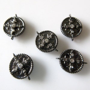 May include: Five black metal round charms with a decorative design and clear rhinestones. Each charm has two loops for attaching to a necklace or bracelet.
