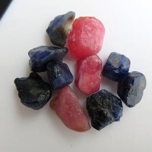 Puede incluir: Un grupo de piedras preciosas sin pulir. Hay ocho piedras en total, cinco son zafiros azules y tres son rubíes rosas.