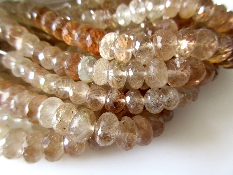 May include: A strand of faceted, translucent brown gemstone beads. The beads are round and have a slightly irregular shape. The beads are strung on a clear thread.