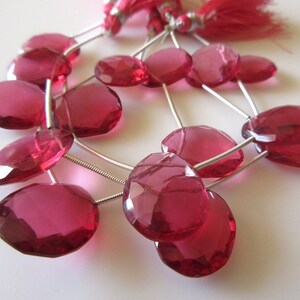 May include: A strand of pink faceted gemstone beads with silver wire loops. The beads are oval shaped and have a translucent appearance.