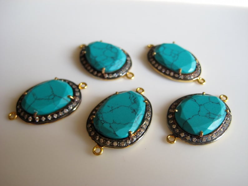 May include: Five turquoise gemstone connector pieces with gold and silver accents. Each piece has a turquoise stone surrounded by a silver bezel and a gold rim. The stones are oval shaped and have a mottled pattern.