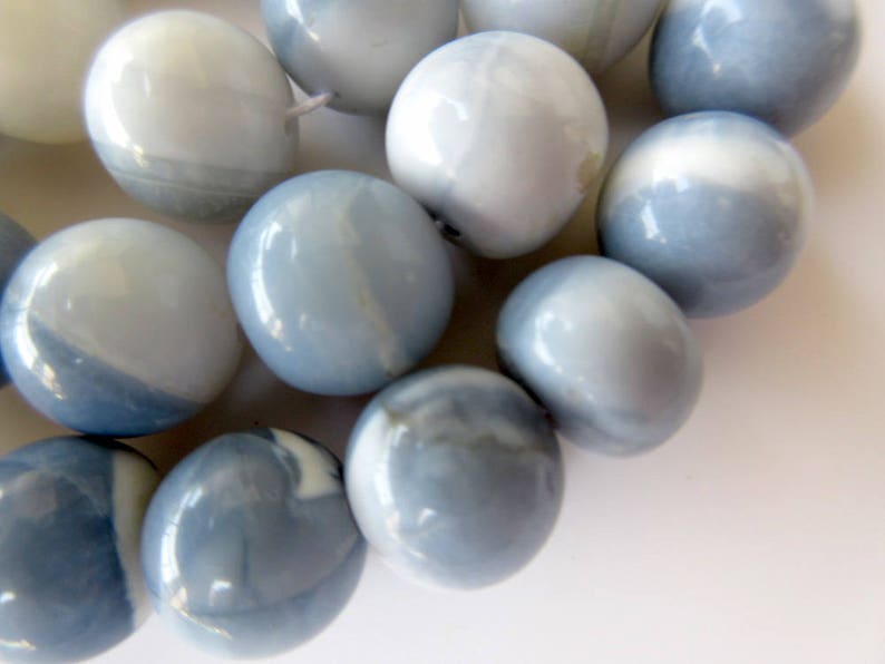 May include: A strand of round, blue and white opal beads. The beads have a smooth, polished finish and a mottled pattern.