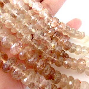 May include: A strand of translucent, faceted, light brown gemstone beads. The beads are round and have a slightly irregular shape.