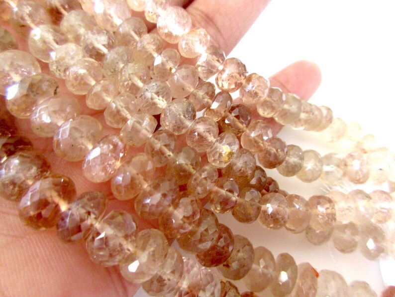 May include: A strand of translucent, faceted, light brown gemstone beads. The beads are round and have a slightly irregular shape.