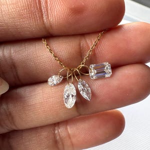 May include: A delicate gold necklace featuring five clear, sparkling gemstones. The necklace has a fine chain and includes a rectangular emerald-cut stone and four smaller, pear and marquise-shaped stones. The gemstones are suspended from small gold hoops.