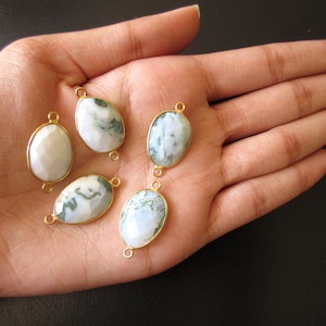 May include: Five oval-shaped agate gemstone beads with gold-toned metal accents. The beads are white with green and gray marbling.