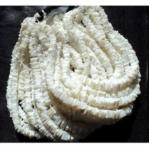 May include: A strand of white shell beads, each bead is rectangular and flat. The beads are strung together to form a long necklace.