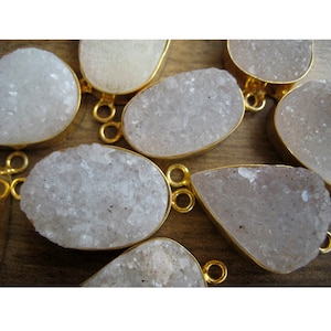 May include: A group of white, crystal-like, teardrop-shaped pendants with gold-toned metal accents. The pendants are arranged on a wooden surface.