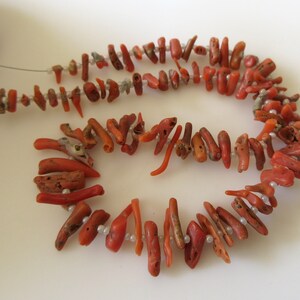May include: A strand of coral beads, featuring a mix of red and orange coral pieces, with a few white beads interspersed throughout.