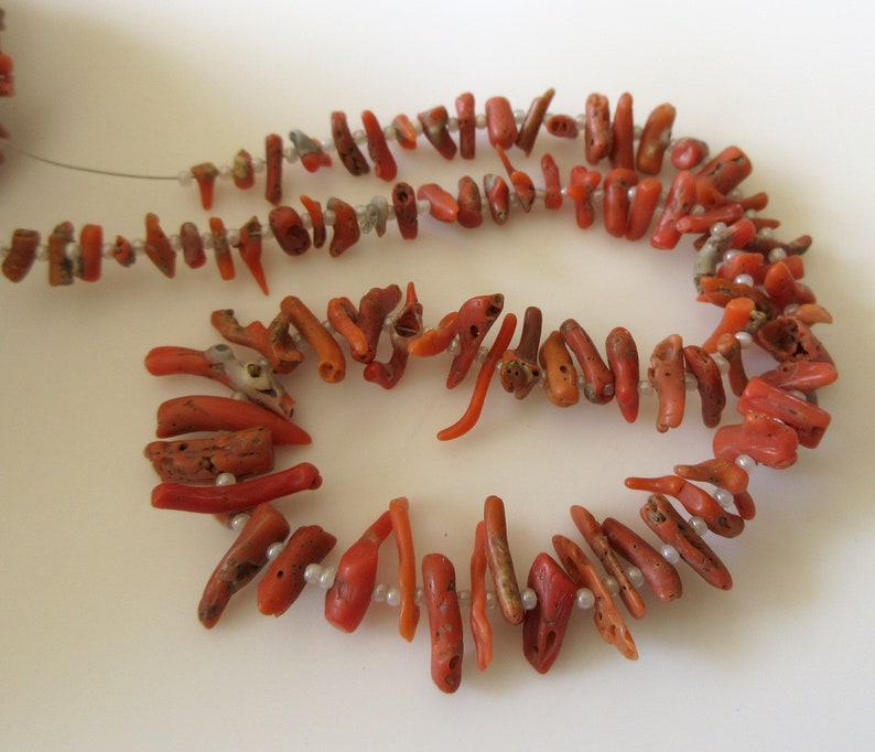 May include: A strand of coral beads, featuring a mix of red and orange coral pieces, with a few white beads interspersed throughout.