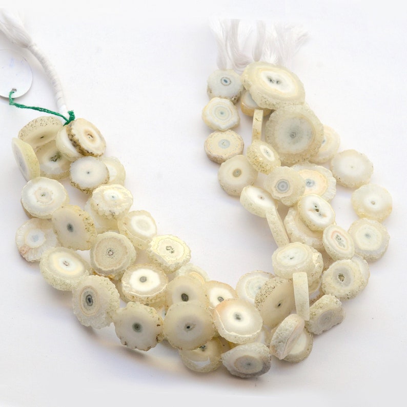 May include: A strand of white agate beads with a crystal-like appearance. The beads are round and have a flat, circular shape. The beads are strung on a white cord.