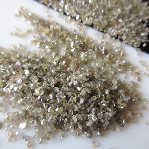 May include: A pile of small, rough, light brown diamonds. The diamonds are scattered on a white surface.