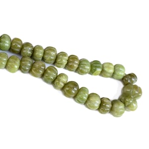 以下が含まれることがあります： 彫刻されたかぼちゃの形をした緑色の宝石ビーズの糸。ビーズは透明な糸に通され、緩やかな流れのあるパターンで配置されています。