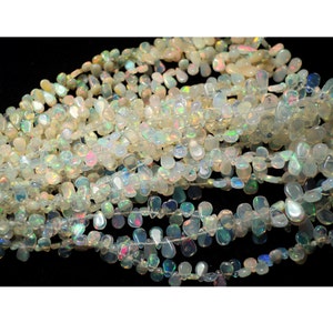 May include: A strand of white opal gemstone beads in a teardrop shape. The beads are iridescent and have a rainbow sheen.