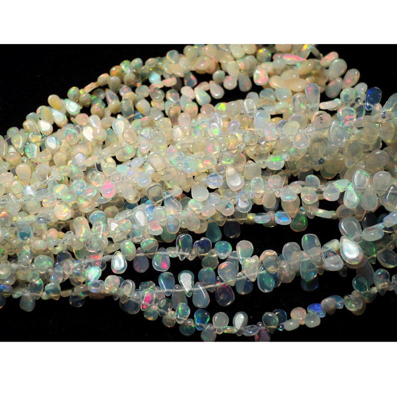 May include: A strand of white opal gemstone beads in a teardrop shape. The beads are iridescent and have a rainbow sheen.