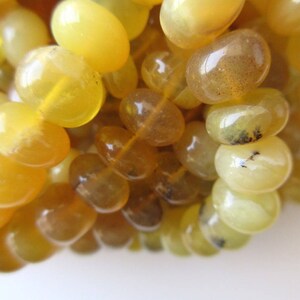 May include: A strand of yellow opal beads, each bead is smooth and oval shaped. The beads have a translucent quality and some have a slight brown tint.