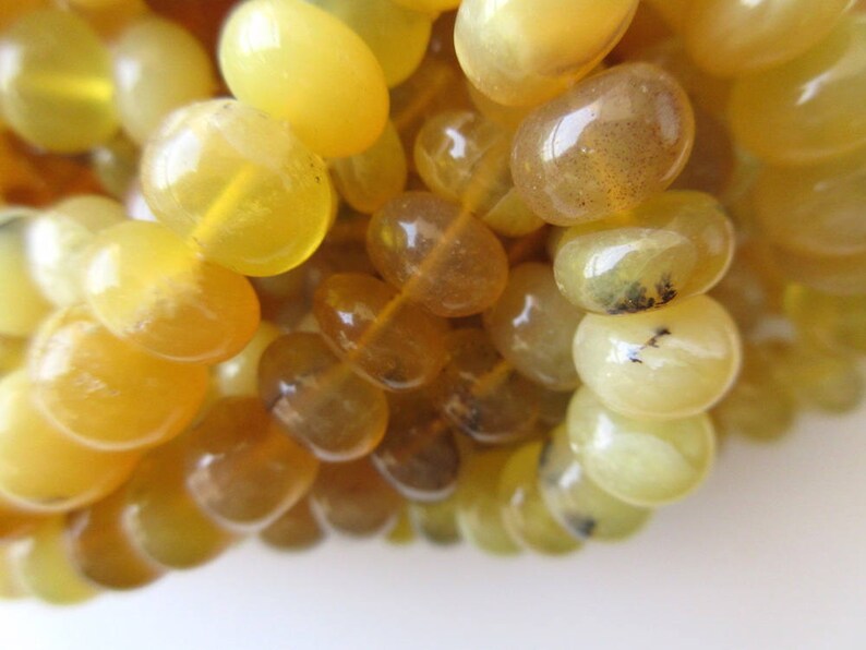 May include: A strand of yellow opal beads, each bead is smooth and oval shaped. The beads have a translucent quality and some have a slight brown tint.