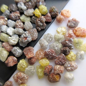 May include: A collection of rough, uncut diamonds in various colors, including clear, yellow, brown, and red. The diamonds are scattered on a black and white surface.