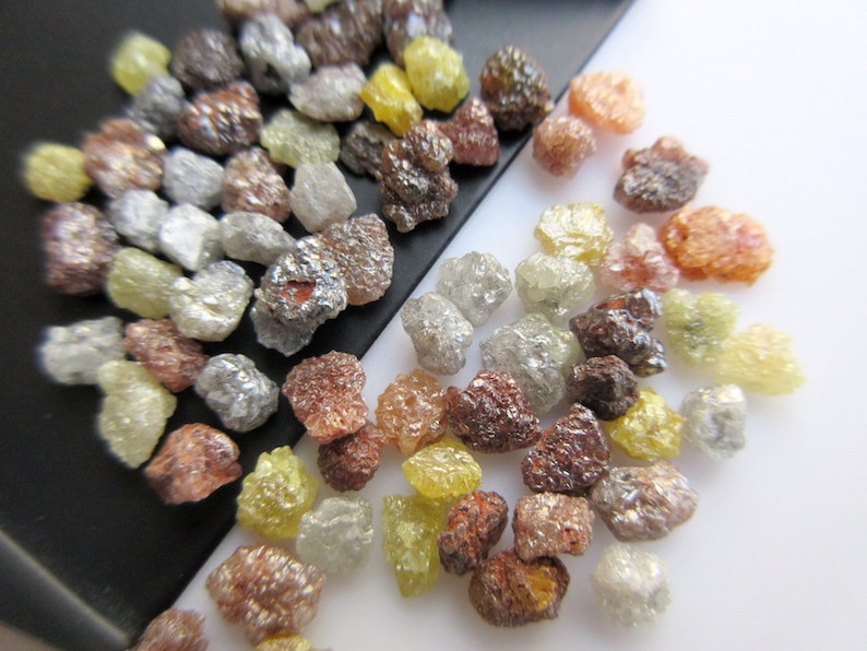 May include: A collection of rough, uncut diamonds in various colors, including clear, yellow, brown, and red. The diamonds are scattered on a black and white surface.