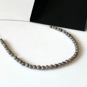 May include: A strand of round, gray beads with a speckled texture, strung on a silver wire.