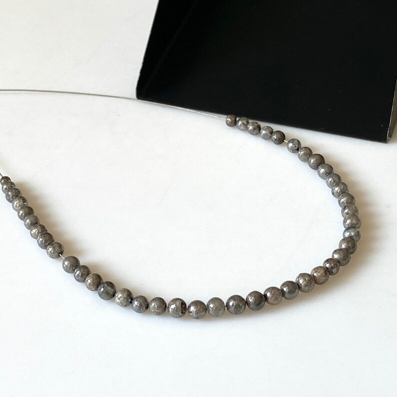 May include: A strand of round, gray beads with a speckled texture, strung on a silver wire.