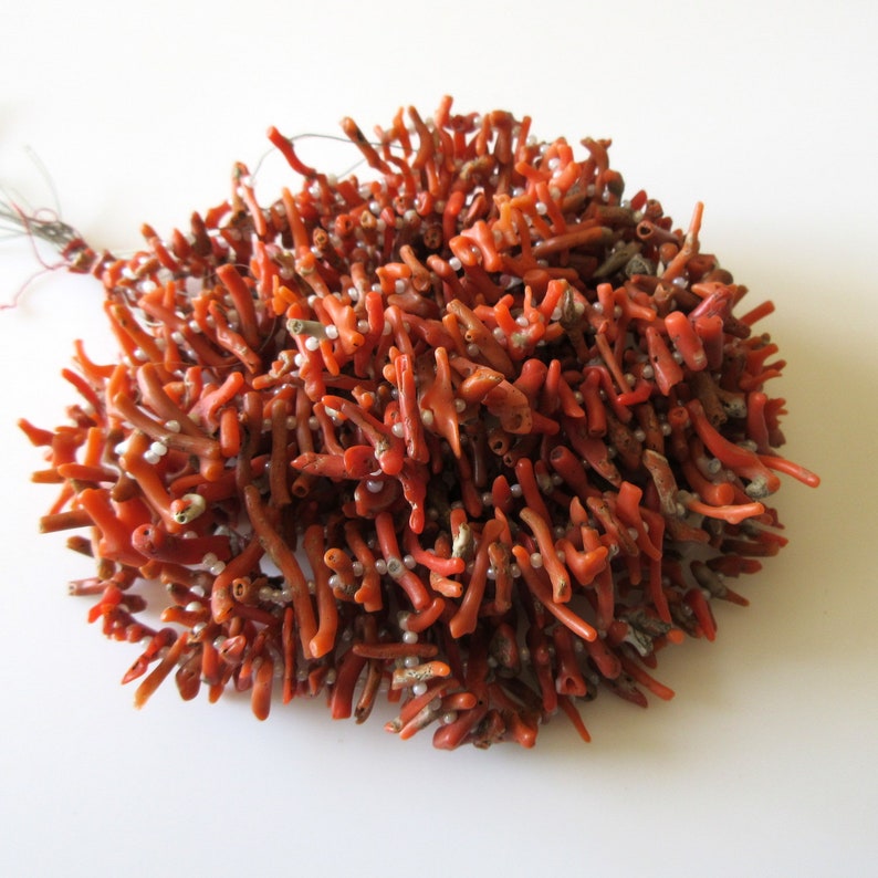 May include: A strand of red coral beads with small white beads interspersed throughout. The coral is a natural, branch-like shape.