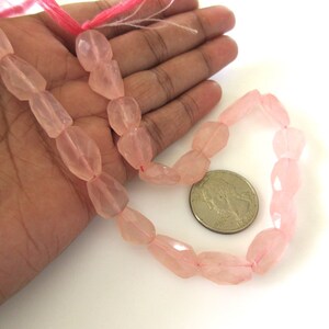 May include: A strand of pink rose quartz beads, faceted and strung on a pink thread. The beads are approximately 1/2 inch in size and are displayed on a hand for size reference.