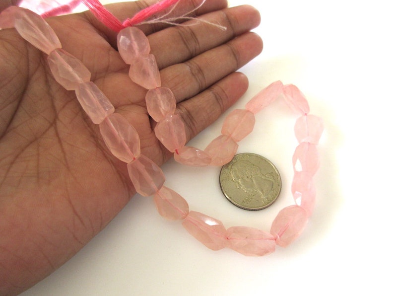 May include: A strand of pink rose quartz beads, faceted and strung on a pink thread. The beads are approximately 1/2 inch in size and are displayed on a hand for size reference.