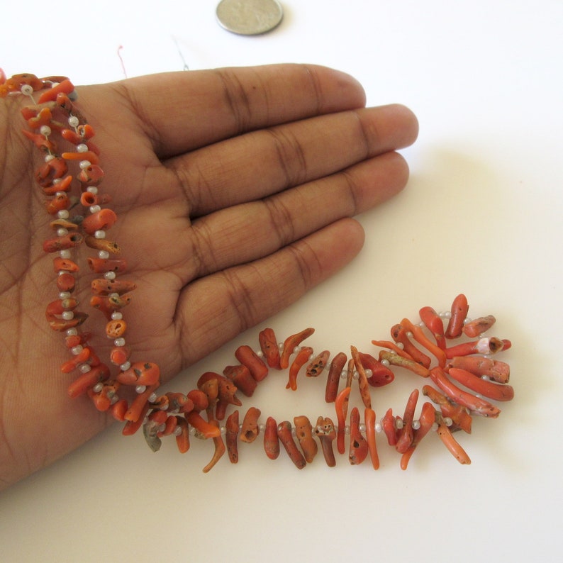 May include: A strand of orange coral beads with small white beads interspersed throughout. The coral beads are irregular in shape and have a rough texture.