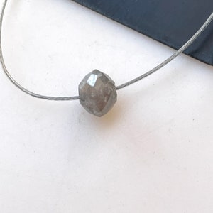 Op de afbeelding: Een enkele, grijze, gefacetteerde diamantkraal op een zilveren draad.