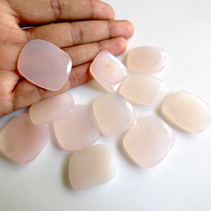 May include: A collection of ten pale pink, smooth, polished, rectangular-shaped stones. The stones are arranged on a white surface.