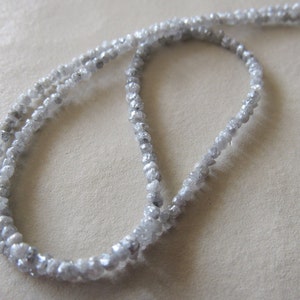 May include: A strand of white rough diamond beads, strung on a white cord. The beads are irregular in shape and size, and they have a natural, unpolished look.