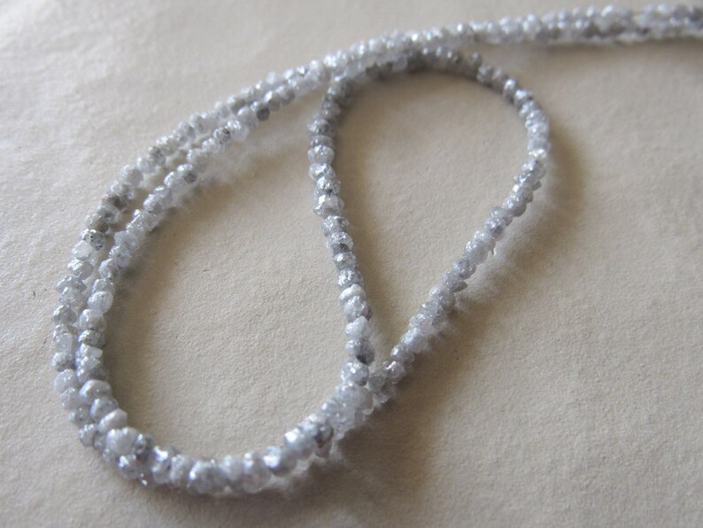 May include: A strand of white rough diamond beads, strung on a white cord. The beads are irregular in shape and size, and they have a natural, unpolished look.