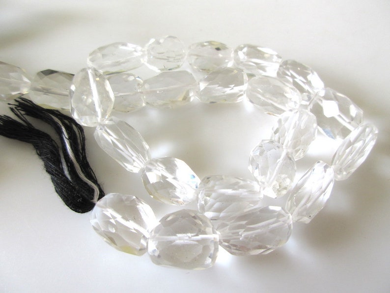 K&ouml;nnte beinhalten: Eine Kette aus klaren Quarzkristallperlen, jede Perle ist facettiert und oval geformt. Die Perlen sind auf einer schwarzen und wei&szlig;en Schnur mit einem Quasten aufgef&auml;delt.