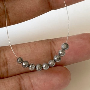 May include: A strand of silver beads with a speckled, metallic finish. The beads are round and have a slightly irregular shape. The beads are strung on a clear thread.