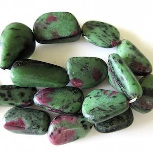 Puede incluir: Una hebra de cuentas de piedras preciosas verdes y rosas. Las cuentas son lisas y pulidas, con una forma natural irregular.