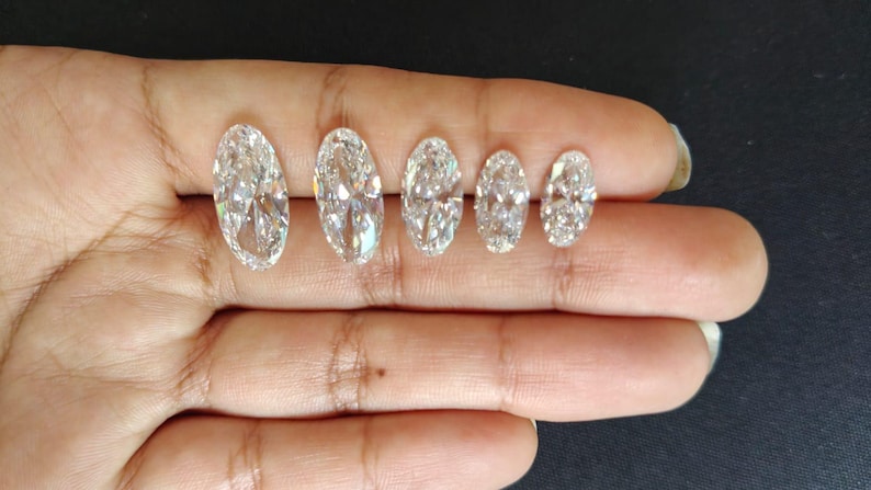 May include: Five clear, colorless, oval-cut gemstones arranged in a row by size from largest to smallest. Each stone features a faceted surface that reflects light, creating a brilliant, sparkling appearance with multiple internal light refractions.