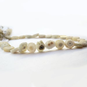 May include: A strand of white agate beads with a green and brown crystal pattern. The beads are round and have a smooth, polished surface.