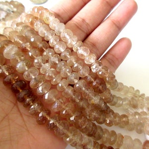 May include: A strand of light brown faceted gemstone beads. The beads are round and have a smooth, polished finish. The beads are strung on a clear thread.