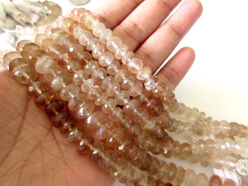 May include: A strand of light brown faceted gemstone beads. The beads are round and have a smooth, polished finish. The beads are strung on a clear thread.