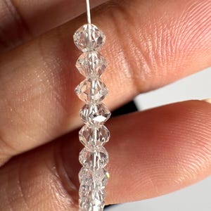 Puede incluir: Un hilo de cuentas de cristal transparente y facetado. Las cuentas est&aacute;n ensartadas en un fino alambre plateado. Los cristales tienen forma de diamante y reflejan la luz, creando un efecto brillante. Las cuentas se sostienen sobre un fondo borroso.