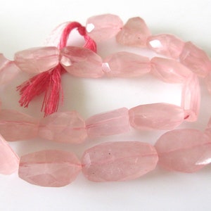 May include: A strand of pale pink rose quartz beads, each bead is faceted and has a slightly irregular oval shape. The beads are strung on a thin cord with a pink tassel.