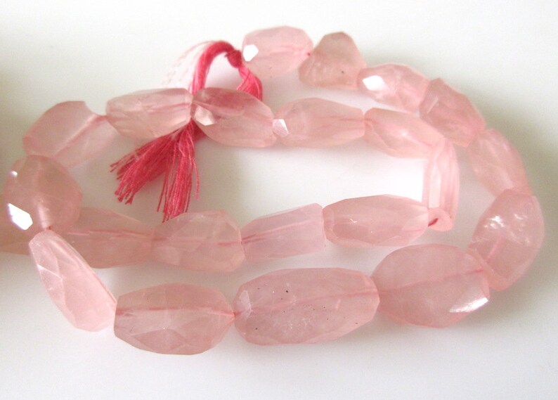 May include: A strand of pale pink rose quartz beads, each bead is faceted and has a slightly irregular oval shape. The beads are strung on a thin cord with a pink tassel.