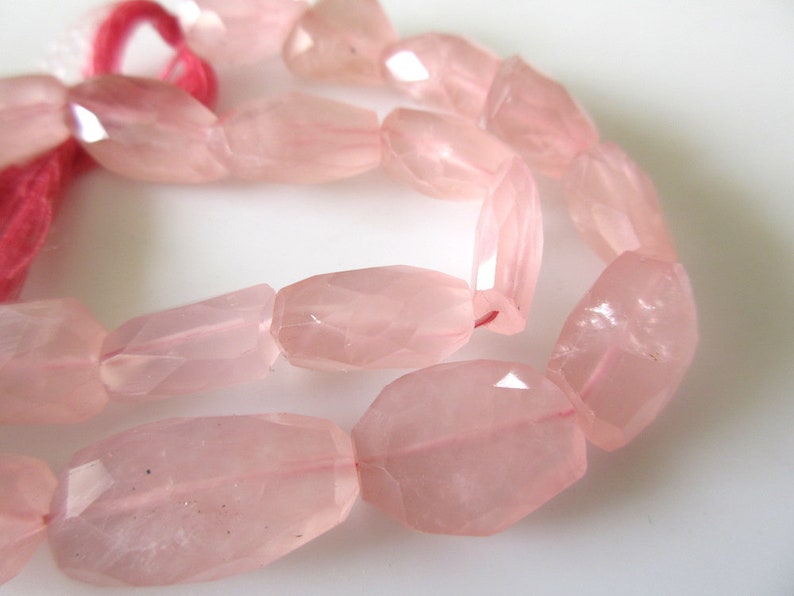 May include: A strand of pale pink rose quartz beads, each bead is faceted and has a slightly irregular oval shape.