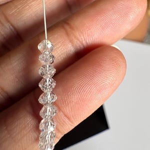 Puede incluir: Una delicada hebra de cuentas de cristal transparente. La hebra presenta m&uacute;ltiples cuentas de cristal facetadas ensartadas en un fino alambre plateado. Las cuentas se mantienen unidas por un peque&ntilde;o cristal redondo en la parte superior. Los cristales brillan.