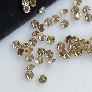 May include: A collection of small, round, brown diamonds scattered on a white surface. The diamonds are of various sizes and have a slight sparkle.