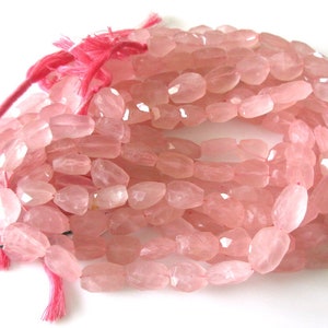 May include: A strand of pink rose quartz beads, faceted and oval shaped. The beads are strung on a pink thread with green string accents.