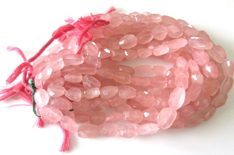 May include: A strand of pink rose quartz beads, faceted and oval shaped. The beads are strung on a pink thread with green string accents.